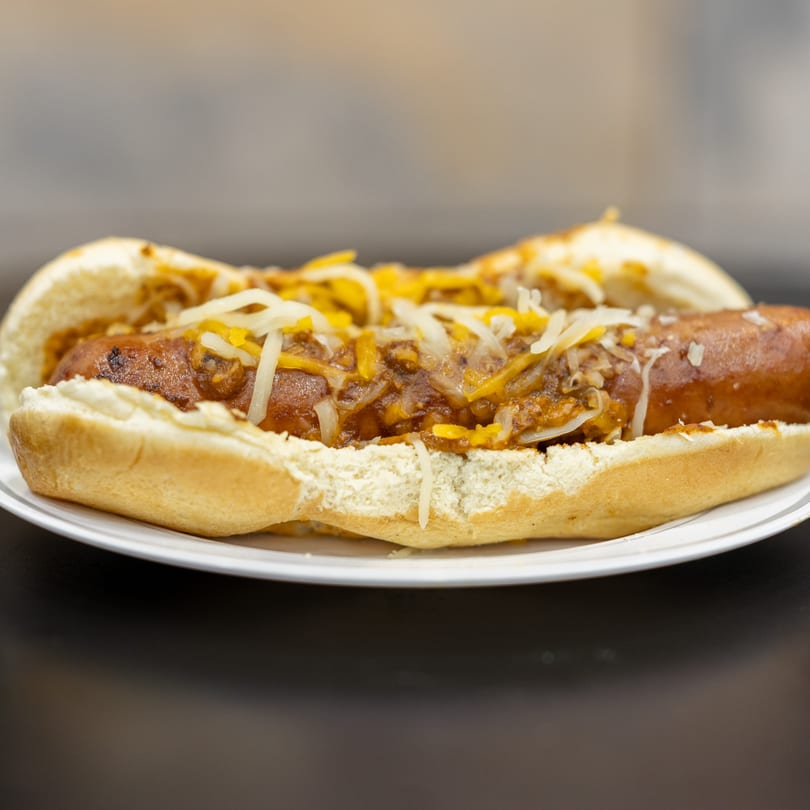 A chili cheese hot dog from You Gotta Eat Here! on a white paper plate.