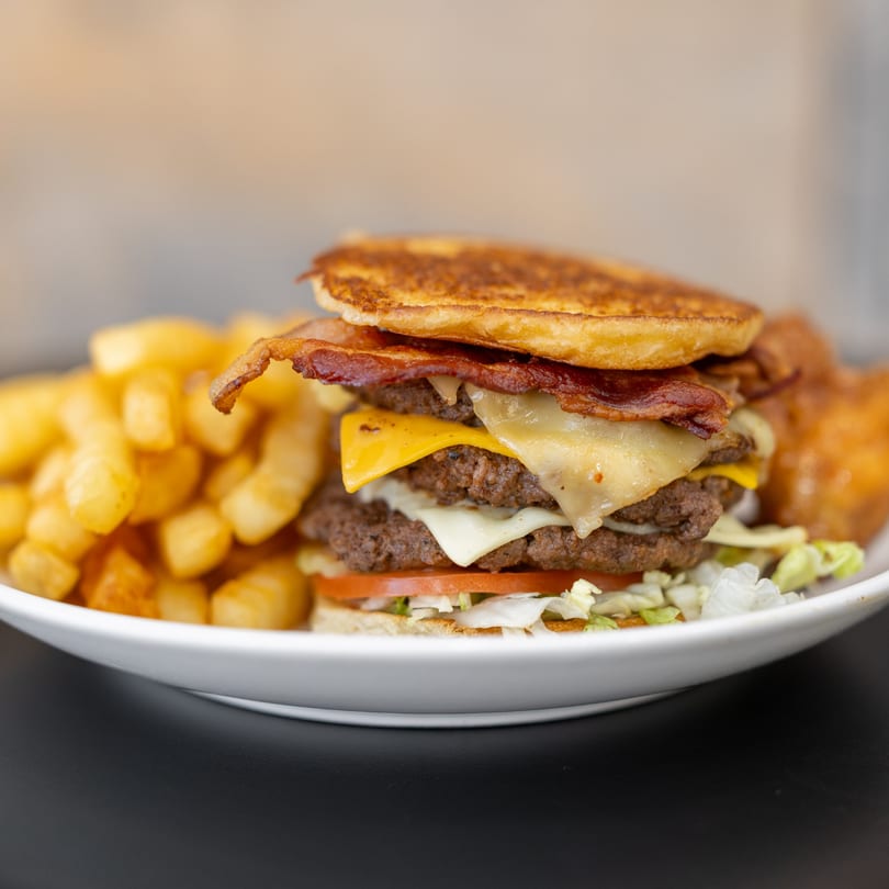 A double cheeseburger with bacon, lettuce, tomato, and a side of golden french fries.