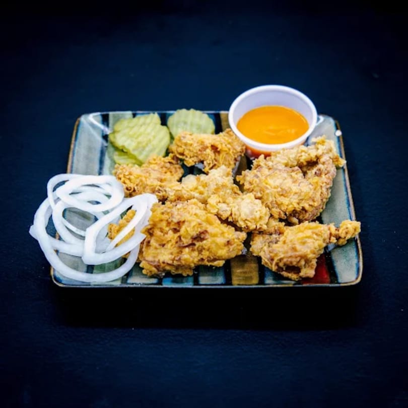 Crispy fried chicken pieces with sliced onions, pickles, and a side of orange dipping sauce.