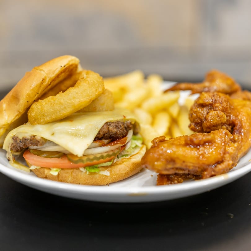 A cheeseburger with onion rings, fries, and chicken wings on a white plate.